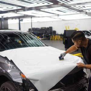 pexels-photo-10126665-10126665 Man applying vinyl wrap on car hood in an automotive workshop setting.